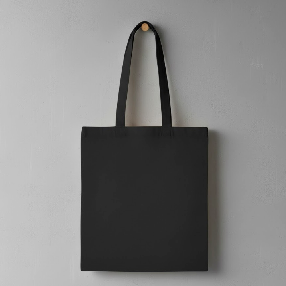 Czarna, prosta materiałowa torba na ramię bez nadruku, zawieszona na drewnianym haczyku na szarej ścianie