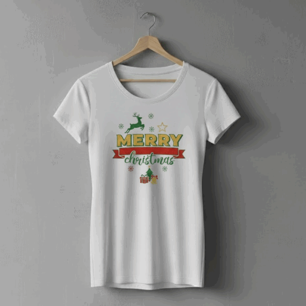 Biała damska koszulka wisząca na drewnianym wieszaku na szarej ścianie. Na koszulce nadruk „Merry Christmas” w zielono-złoto-czerwonych kolorach, z grafikami renifera, gwiazdki, choinki, prezentów i śnieżynek