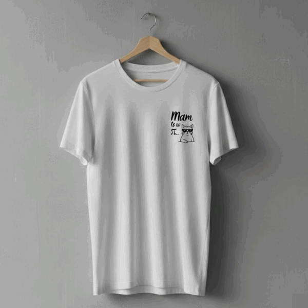 Biała koszulka wisząca na wieszaku na szarej ścianie. Po lewej stronie klatki piersiowej znajduje się czarny nadruk z napisem ‘Mam to w π…’ oraz rysunkiem kota o obojętnym wyrazie twarzy