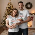 Uśmiechnięci rodzice stojący przed udekorowaną choinką, trzymający śpiące niemowlę; cała trójka ma na sobie białe ubrania z nadrukami ‘Pierwsze Święta jako Mama/Tata/Dziecko’