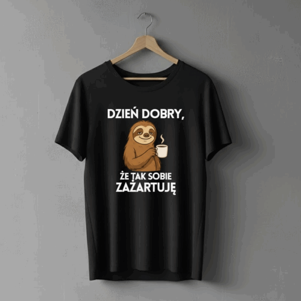 Czarna koszulka wisząca na wieszaku na tle szarej ściany. Na przodzie znajduje się ilustracja uśmiechniętego leniwca trzymającego kubek z parującym napojem oraz biały napis: ‘DZIEŃ DOBRY, ŻE TAK SOBIE ZAŻARTUJĘ’