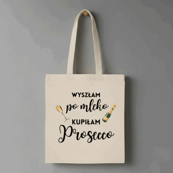 Beżowa materiałowa torba z czarnym napisem: ‘Wyszłam po mleko, kupiłam Prosecco’, ozdobiona rysunkami kieliszka z winem i butelki Prosecco