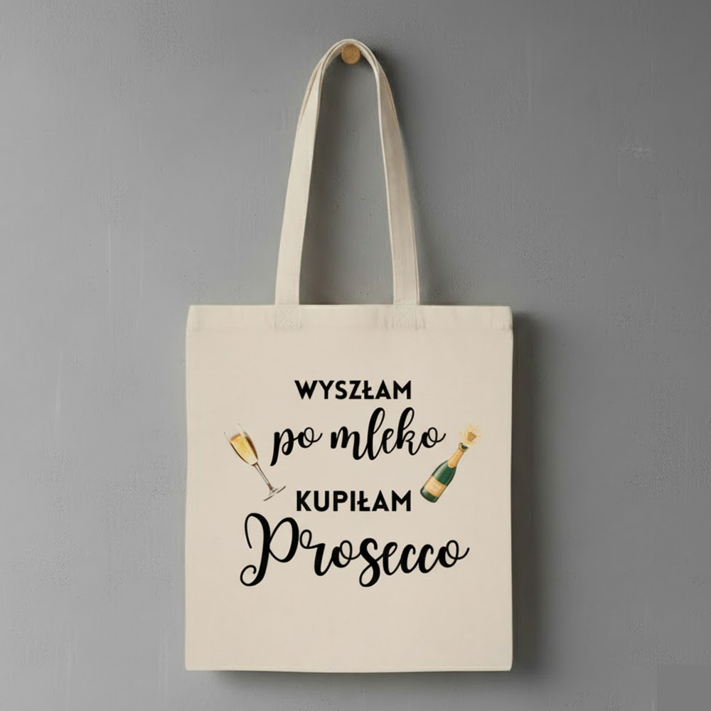 Beżowa materiałowa torba z czarnym napisem: ‘Wyszłam po mleko, kupiłam Prosecco’, ozdobiona rysunkami kieliszka z winem i butelki Prosecco